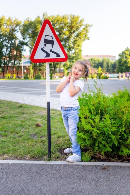 A little child girl stands with a road sign slippery road the concept of traffic rules