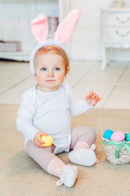 Little child girl wearing bunny ears on Easter day and playing with painted eggs