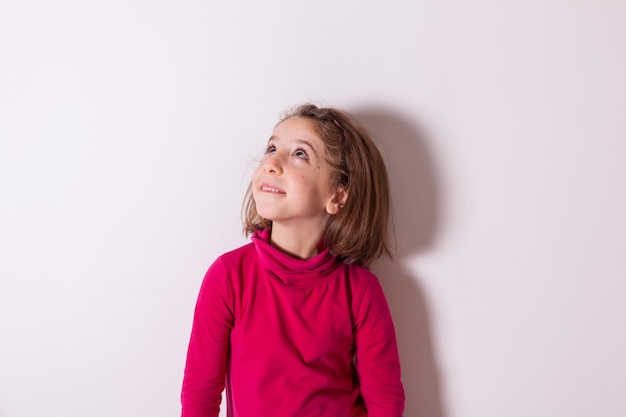 Bambina che indossa collo polo rosso o collo alto sorridente e alzando lo sguardo su sfondo bianco