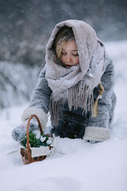 写真 小さな女の子がバスケットを持って雪の下の森で最初の花を探します - ガジェット通信 getnews