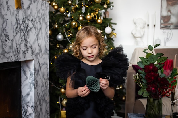 Photo little child girl with christmas present in her hands near christmas trees with lights merry christmas and happy holidays