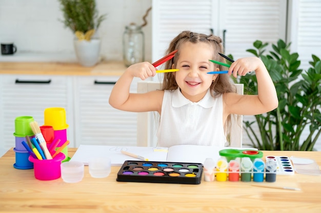 a little child girl with colored pencils learns to draw by playing a girl plays around and has fun in a drawing lesson at an art school and with colored pencils and paints