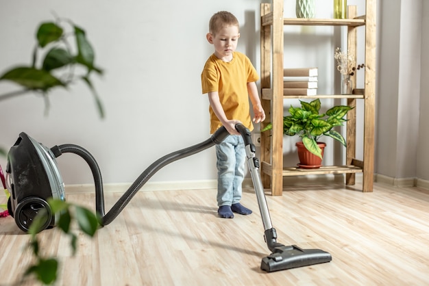 Un bambino aiuta i suoi genitori nelle faccende domestiche, pulisce il pavimento usando un aspirapolvere