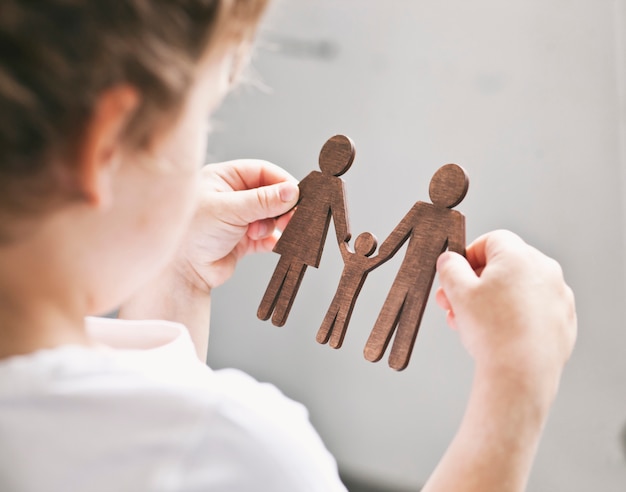 Foto bambino guardando le figure in legno di mamma, papà e bambino nelle sue mani. concetto di bambino che sogna di famiglia