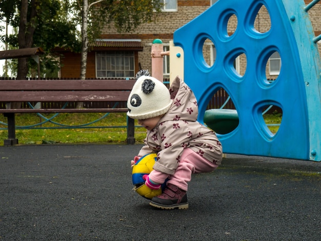 Piccolo bambino che gioca con una palla nel parco giochi in una giornata autunnale