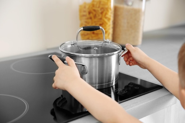 Little child playing with pan and electric stove in the kitchen