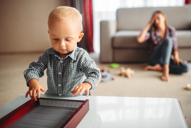 Little child plays in room, stressed mother