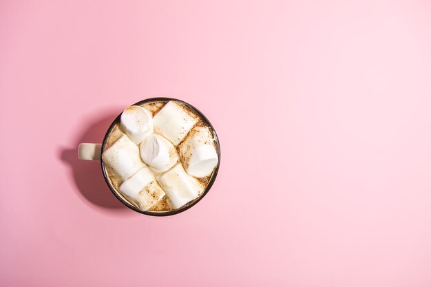 Little child's hands holding ceramic mug with hot fresh cocoa drink with marshmallows on soft pink background.