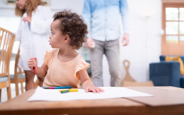 A little child's imagination is represented through colored pencil drawings with the mother attentively supervising in the living room of the house