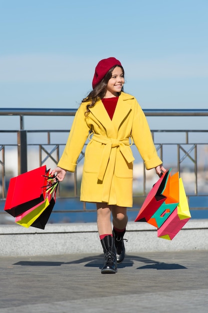 Piccolo bambino shopping autunno saldi stagione bambino adorabile elegante tenere mazzo borse della spesa ragazza carina piccola signora vestita in stile francese cappotto e berretto portare borse della spesa concetto di shopping autunnale