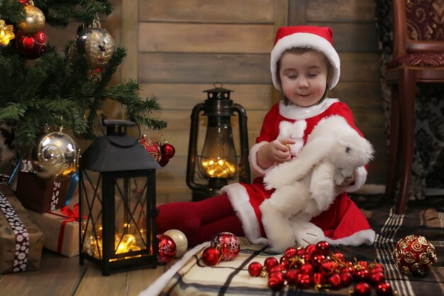 Little child sitting in front of a Christmas tree and playing with toys