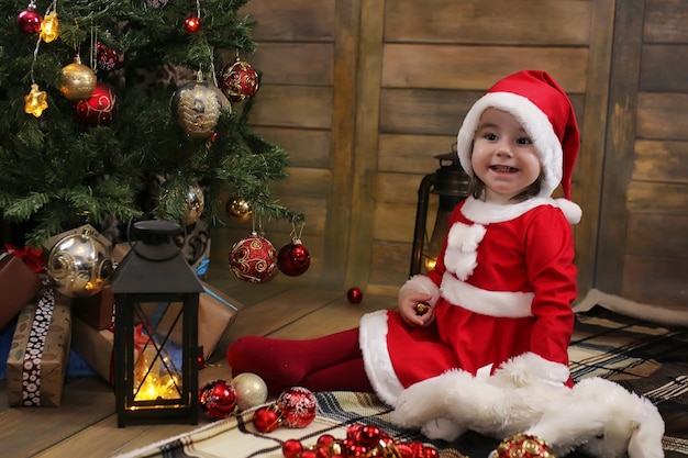 Little child sitting in front of a Christmas tree and playing with toys