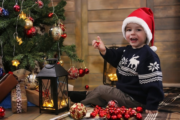 Little child sitting in front of a Christmas tree and playing with toys