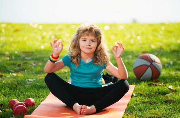 Little child sitting on the roll mat practicing meditate yoga in the park outdoor Kid boy practicing yoga pose