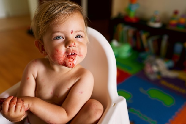 Little child with dirty face sits on a chair arms folded