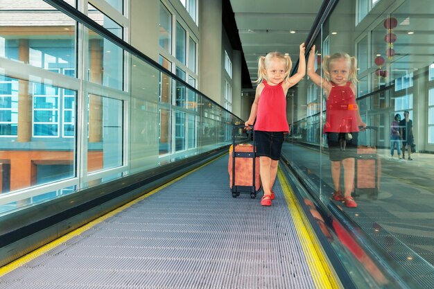 Photo little child with luggage stand on airport transit hall walkway moving to plane departure gate for waiting flight boarding.