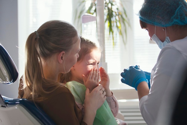 Photo little child with mommy in stomatology chair - girl is crying, close up