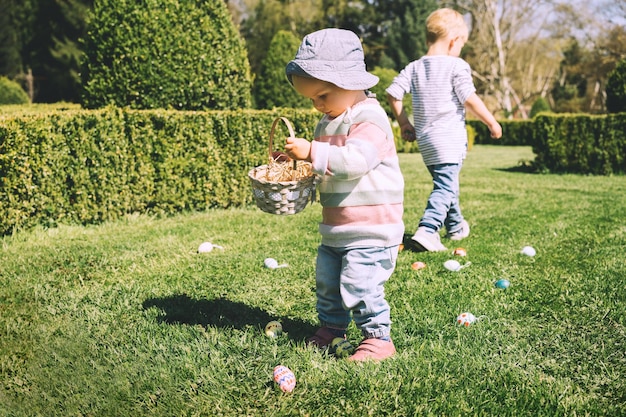 写真 春の公園で塗装された装飾の卵を集める小さな子供たち子供たちは屋外で卵を探しますイースターのお祝いの家族の伝統的な遊びゲームバスケットのカラフルなイースターエッグ