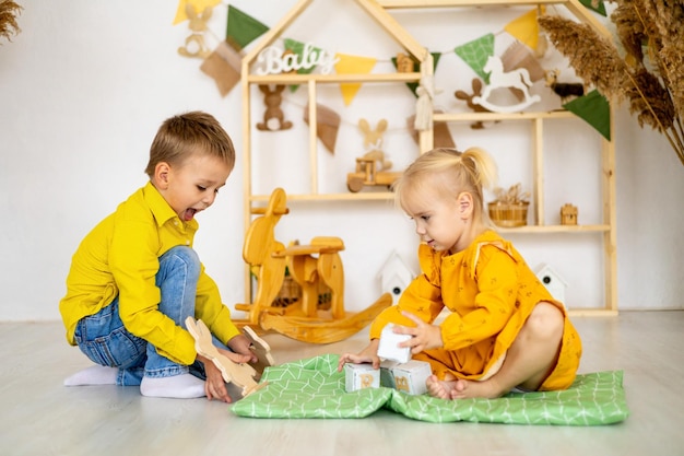 Маленькая девочка с мальчиком и сестрой играют дома с деревянными игрушками, стоят пирамидой или башней и улыбаются счастливому детству