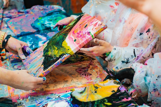 Little children's hands pouring acrylic paint onto a canvas