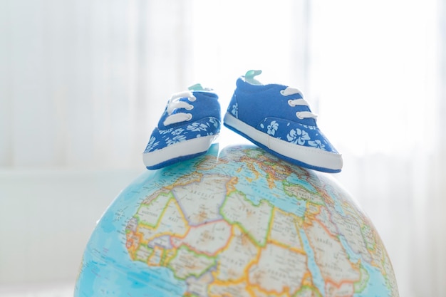 Маленькая детская обувь стоит на глобусе Концепция путешествия и входа в мир маленького человека