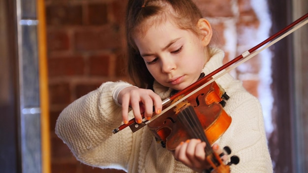 Маленькая сосредоточенная девочка в белом свитере, играющая на скрипке