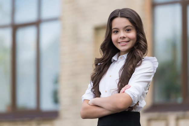 Poco ma fiducioso. il bambino tiene le braccia incrociate all'aperto. la bambina indossa l'uniforme scolastica. di nuovo a scuola. educazione formale. attività di doposcuola. sii giovane e impara a scuola, copia spazio.