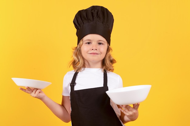Little cook with cooking plate Child chef cook Child wearing cooker uniform and chef hat preparing food studio portrait
