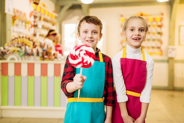 小さな職人が菓子屋で楽しんでいます。手作りのロリポップと幸せな子供たち。焼きたての砂糖キャラメル