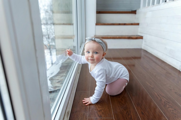 Little crawling baby girl one year old siting on floor in bright light living room near window smili