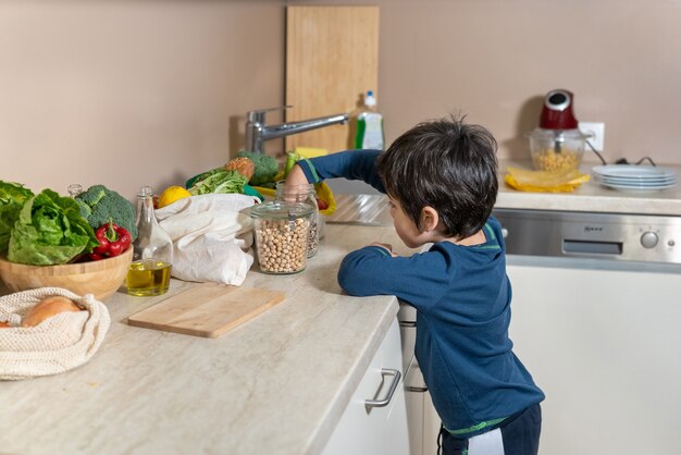 Little curious boy watcheing what is on kitchen table. Zero waste. Eco friendly cotton bags