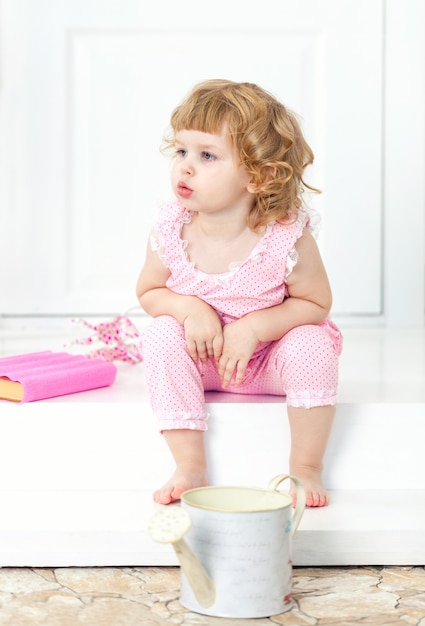 Photo little curly girl in a pink dress sits with thoughtful look and watch into the distance