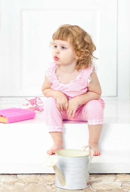 Little curly girl in a pink dress sits with thoughtful look and watch into the distance