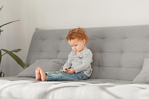 little curly girl using mobile phone while sitting on sofa