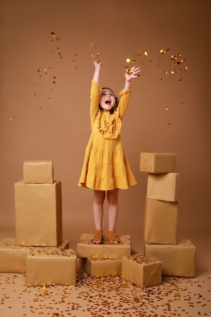 Little curly girl with a stack of gifts for the holiday and gold confetti