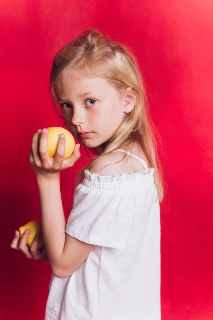 Piccola ragazza adorabile carina con frutta su sfondo rosso