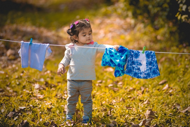 Little cute Asian girl dries clothes in the garden