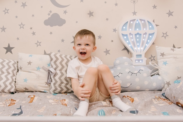 Little cute baby boy sitting in the children room in a wooden bed house with night lights in the shape of a balloon