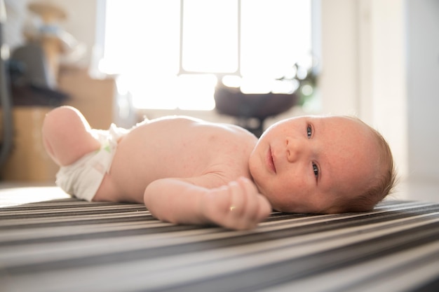 A little cute baby in a diaper restlessly lying on his back on striped sheets in day light