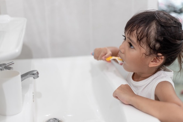 Маленькая милая девочка чистит зубы зубной щеткой в ванной