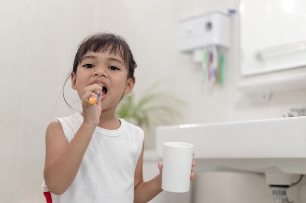 Photo little cute baby girl cleaning her teeth with a toothbrush in the bathroom