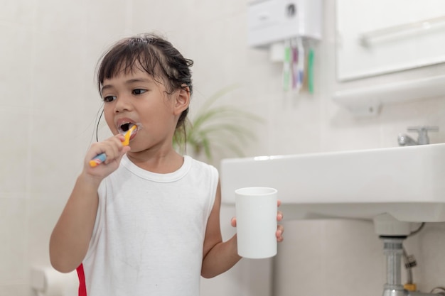 小さなかわいい女の赤ちゃんがバスルームで歯ブラシで歯を掃除
