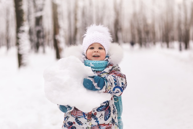 Little cute baby girl holds a big snowball in winter in the park