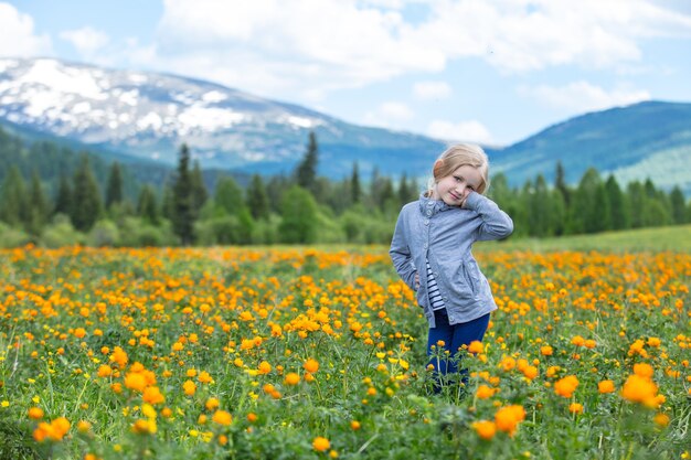 Little cute baby girl is beautiful and happy, smiling in summer in the meadow against the mountains with snow