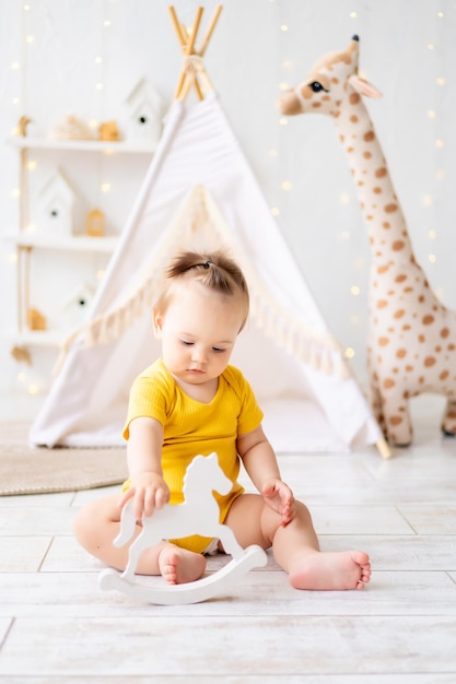 A little cute baby girl is sitting in a bright cozy children's playroom Textiles for children