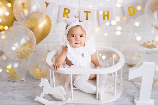 Little cute baby girl sitting with the letters one and balloons, first year, birthday, holiday