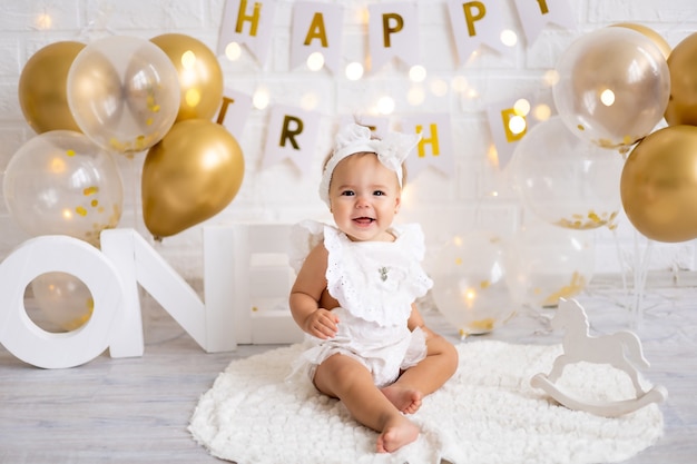 Little cute baby girl sitting with the letters one and balloons, first year, birthday, holiday