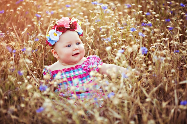 夏の花の牧草地に座っている花の花輪を持つ小さなかわいい女の赤ちゃん