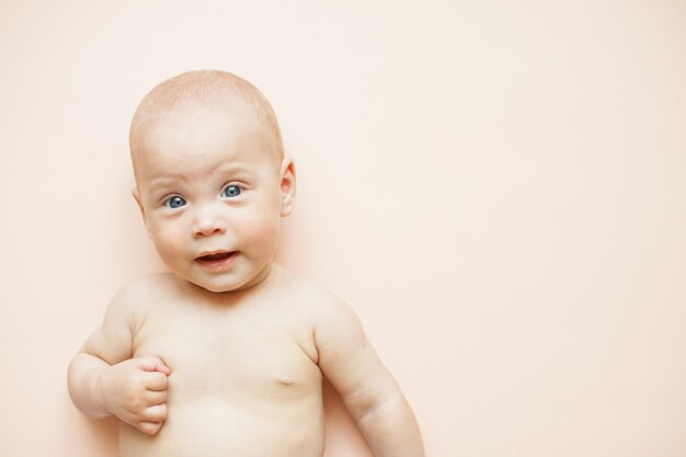 Piccolo bambino carino si trova su uno sfondo rosa chiaro.