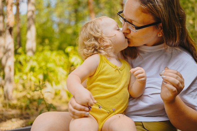 Little cute baby toddler girl blonde with curls on mothers arms mother and daughter kissing playing